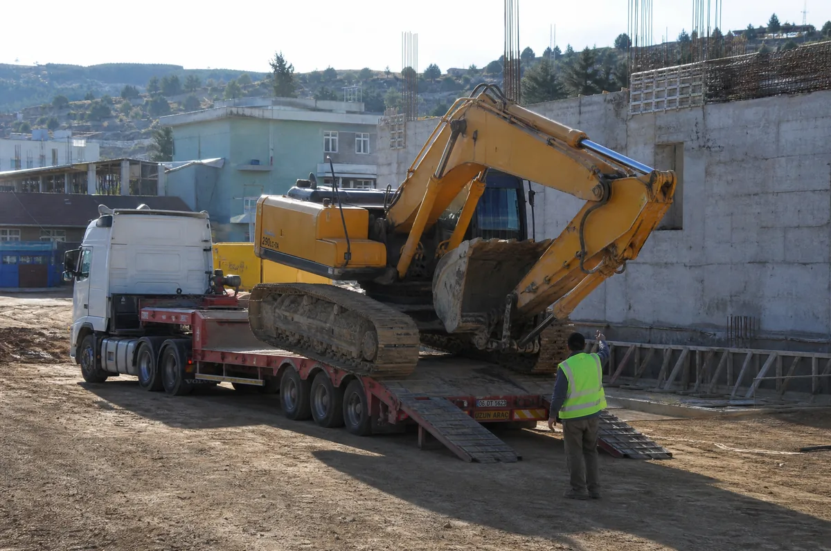 Şantiyede ekskavatörün rampadan lowbed dorseye yüklenmesi, operatör ve yönlendiren sürücü